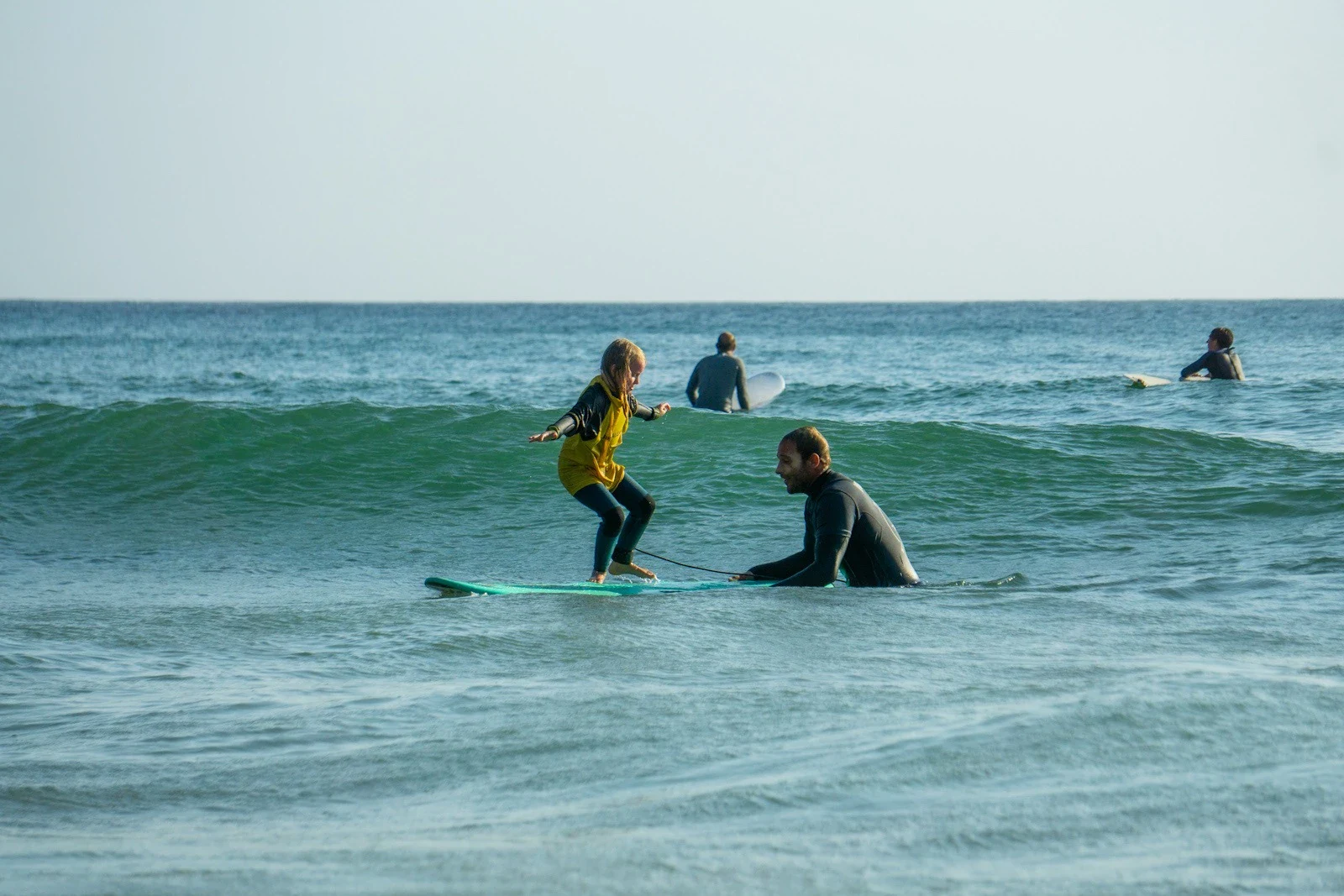 Child standing on surfboard on a green wave with instructor guiding — kids surf lessons Lagos