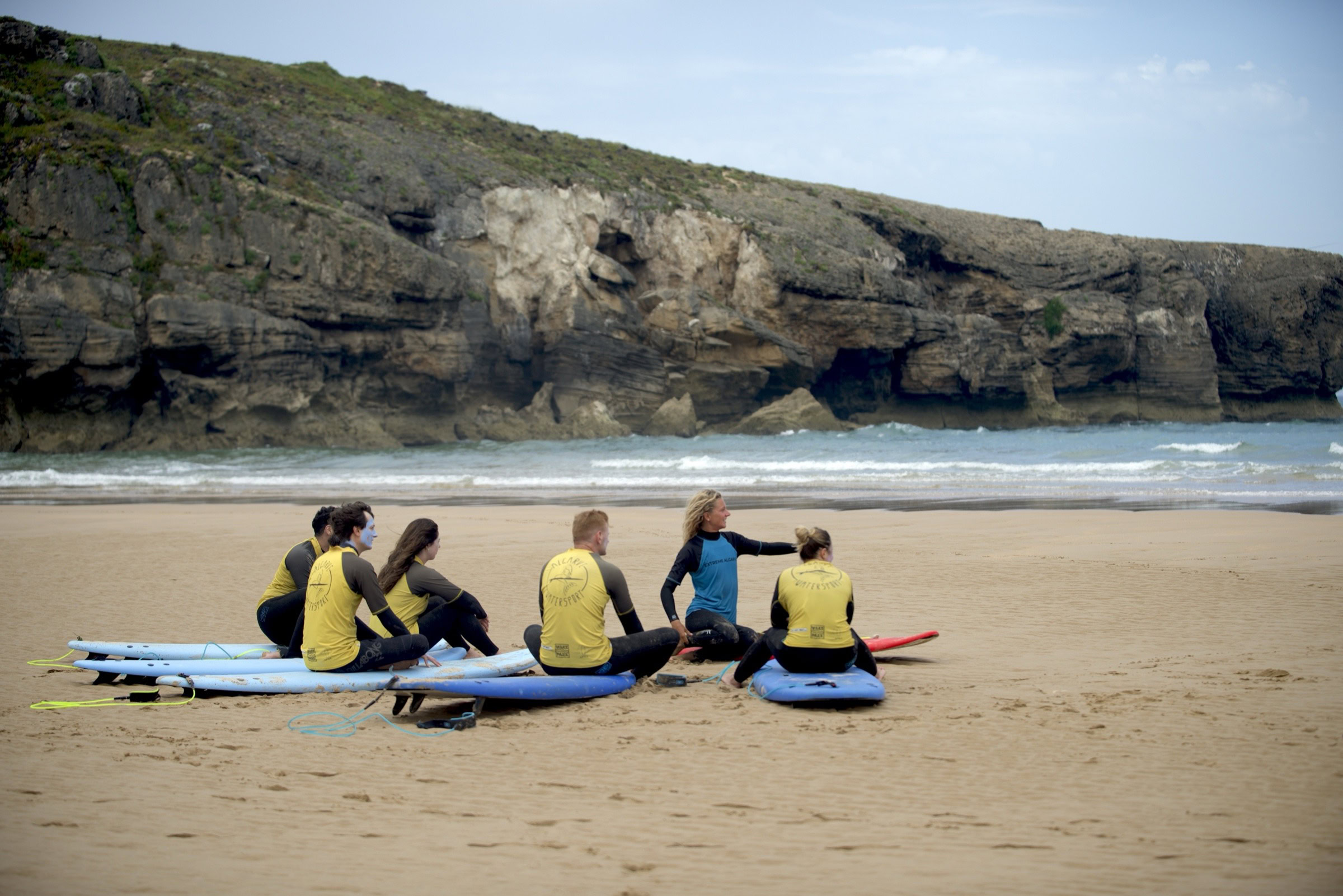 Small group of beginner surfers with instructor on cliff beach in Lagos, Algarve
