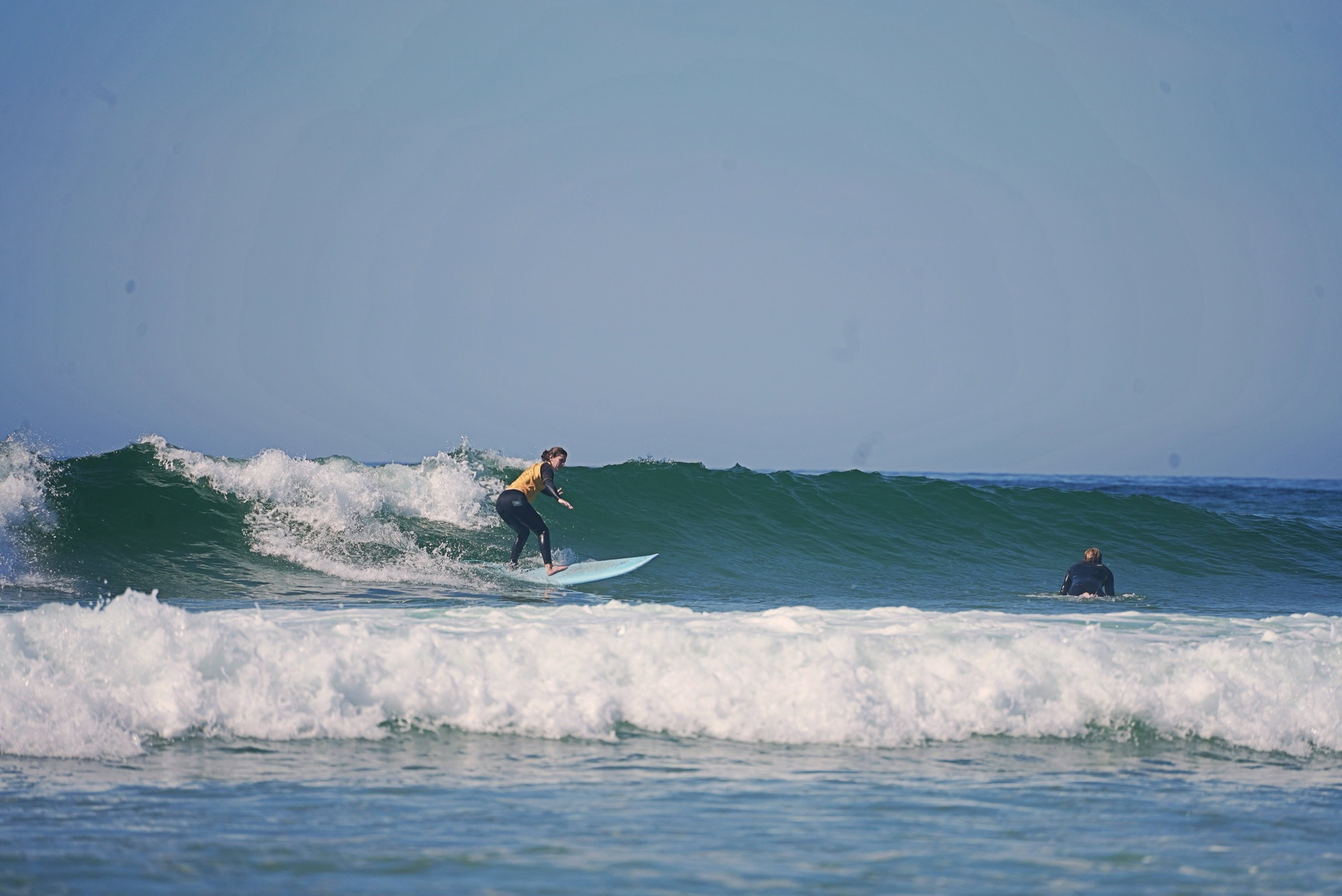 Intermediate surf student riding a green wave in yellow lycra, Algarve