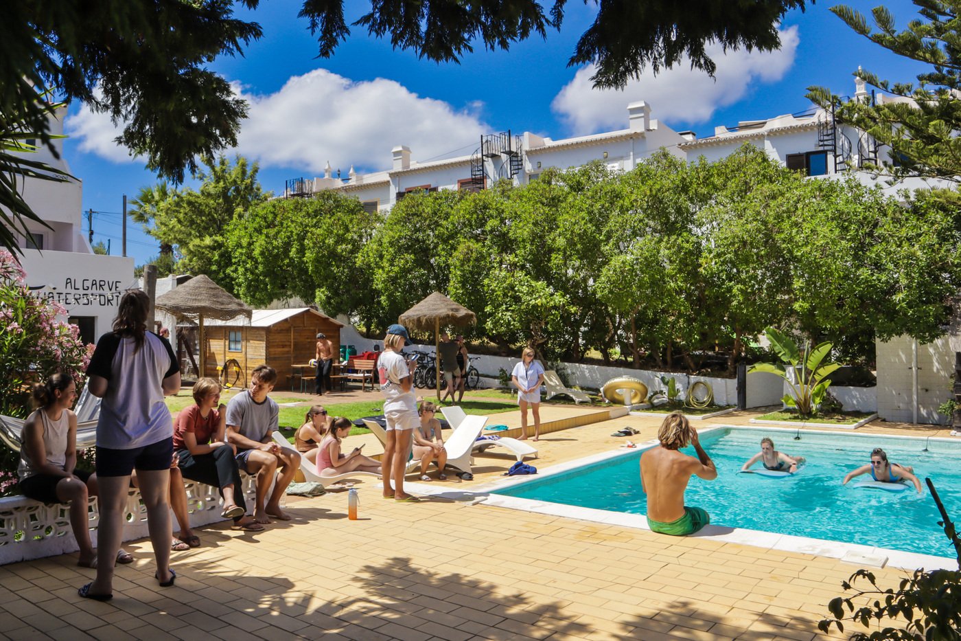 Guests socialising and swimming by the pool on a sunny day at Algarve Watersport surf camp