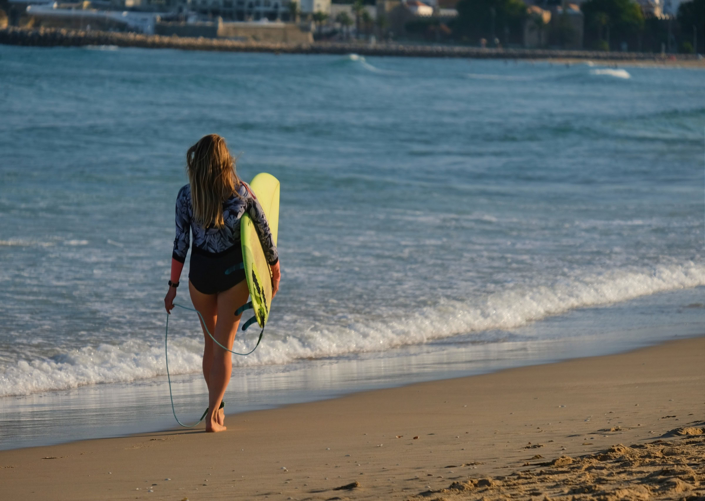 Surfer walking along Meia Praia beach in Lagos, Algarve — surfboard under arm