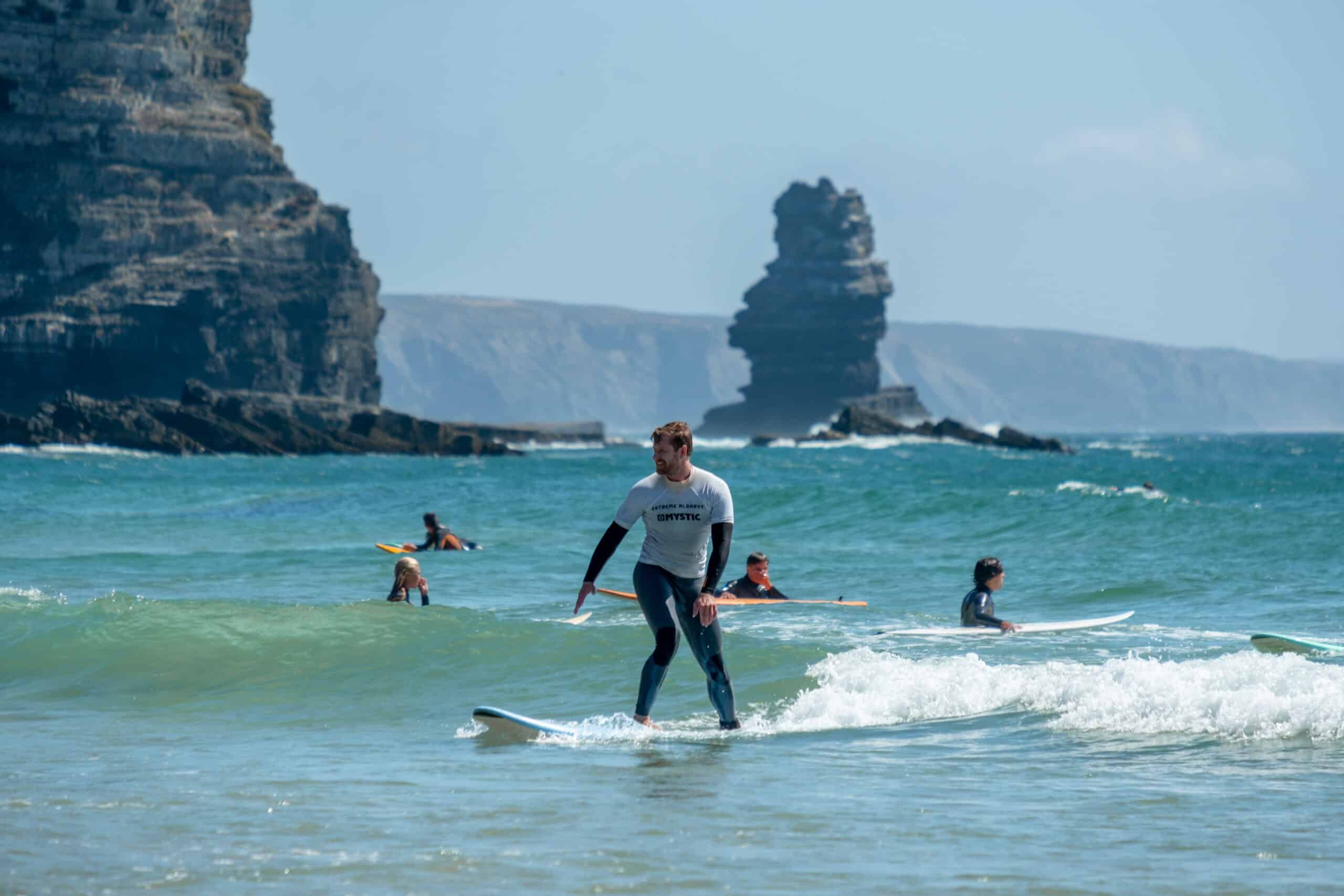 Woman surfing a wave with Algarve cliffs in the background, Lagos Portugal