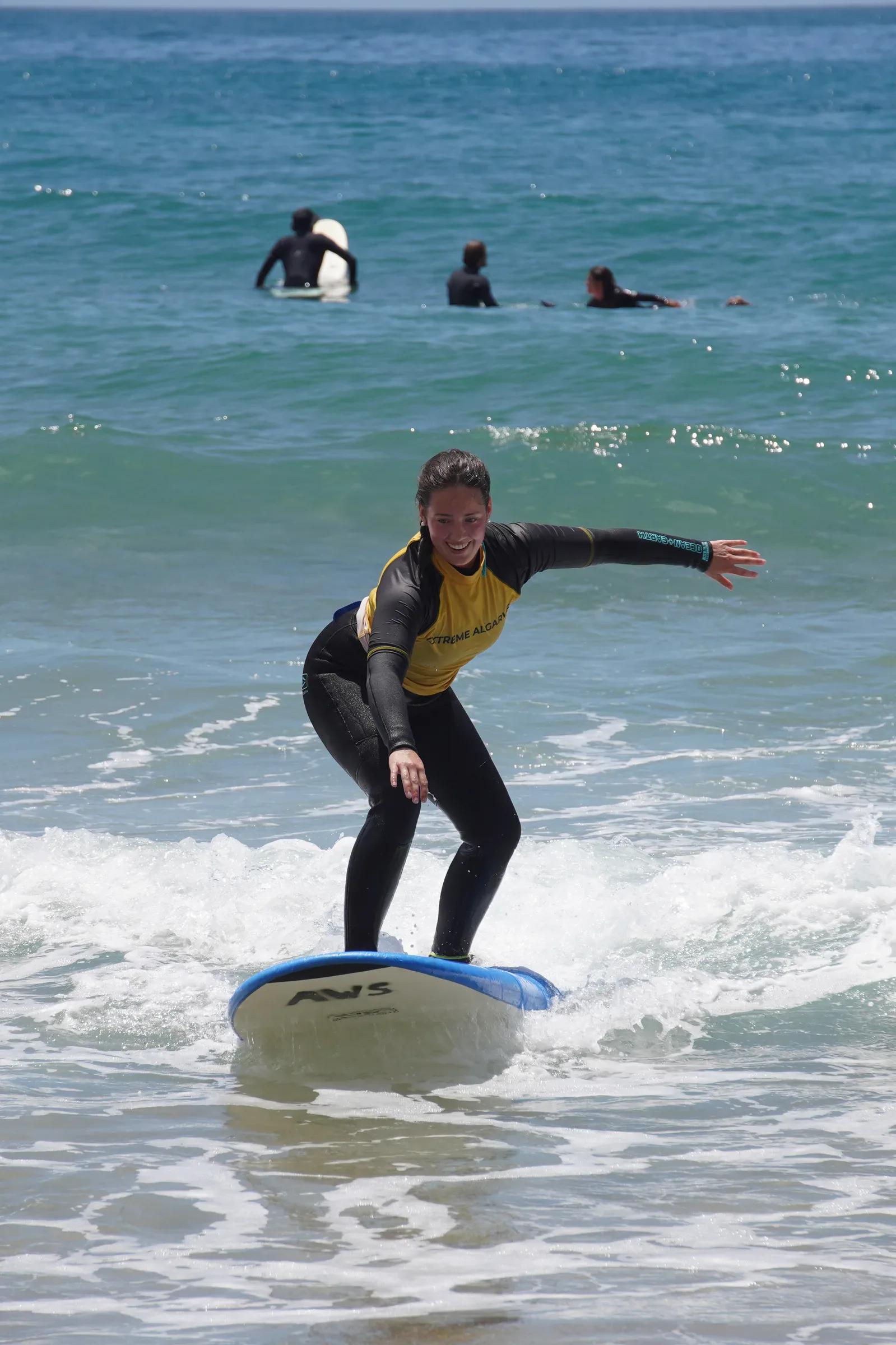 Woman smiling on a foam surfboard in white water during a surf lesson at Algarve Watersport Lagos