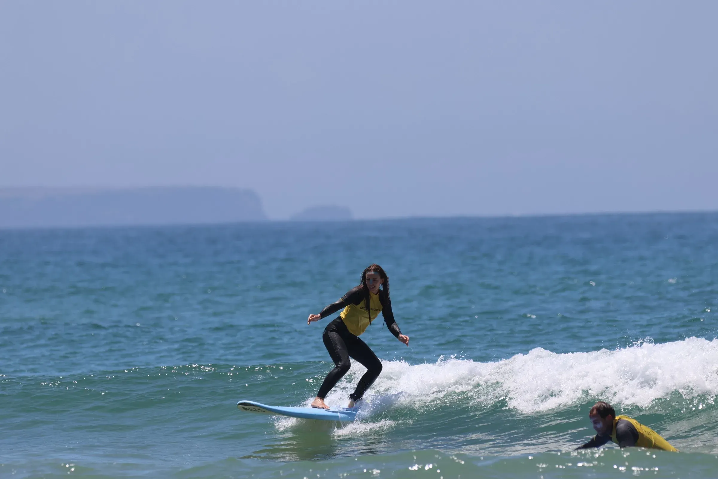Woman surfing a small wave with Algarve cliffs in the background at surf camp Lagos
